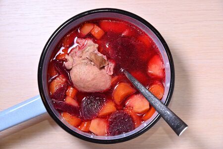 Soup with meat potatoes and beets in a blue ladle with a spoon on a wooden table.の写真素材