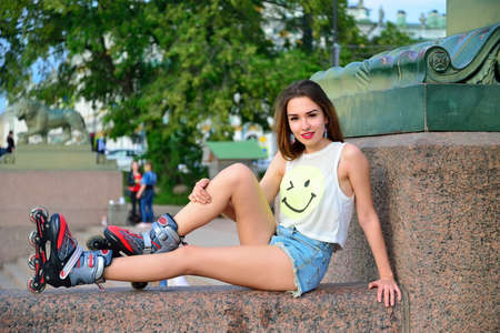 Young girl in roller skates sitting on a granite parapet on the background of sculpture of a lion in St. Petersburgの写真素材