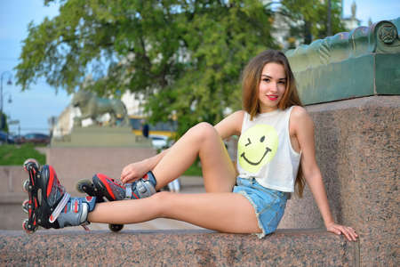 A young girl in roller skates resting on a granite parapet on the background of the sculpture of a lion in St. Petersburg.の写真素材