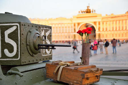Red carnations in a gun case and box of shells at a small Soviet amphibious tank T-38 in the background of the Headquarters  Archの写真素材