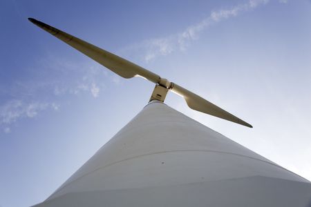A single power generationg windmill against blue sky.