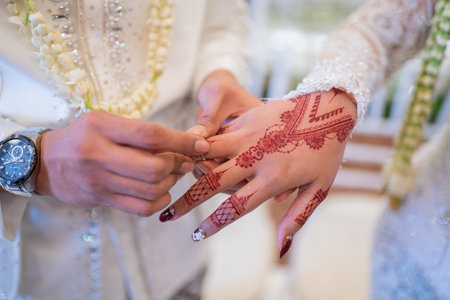 A husband and wife put each other's wedding rings in a traditional Indonesian wedding ceremony. The groom puts a ring on his beloved wife's finger. The couple exchanged wedding rings. Just marriedの写真素材