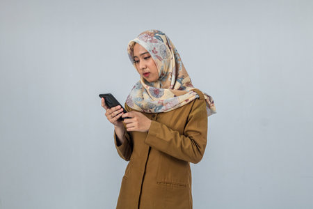 Young Indonesian Woman government employee wearing a brown uniform holding and looking to smartphone on isolated white backgroundの写真素材