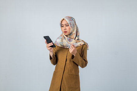 Young Indonesian Woman government employee wearing a brown uniform while holding mobile phone with fist handの写真素材