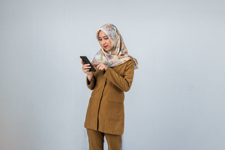 Young Indonesian Woman government employee wearing a brown uniform while pointing his finger to mobile phoneの写真素材