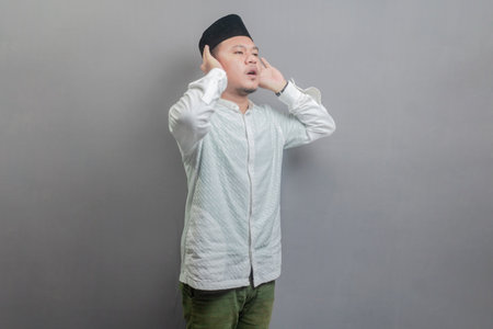 Asian Muslim man wearing a koko shirt and peci with shades of the fasting month, standing reciting...
