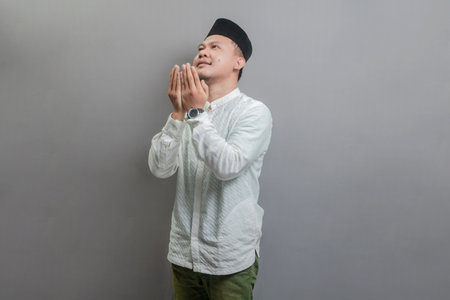 Asian Muslim man wearing a koko shirt and peci with shades of the fasting month, standing looking empty space happily to show grateful , isolated on a gray backgroundの写真素材
