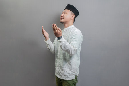 Asian Muslim man wearing a koko shirt and peci with shades of the fasting month, standing looking empty space happily to show grateful , isolated on a gray backgroundの写真素材