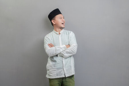 Asian Muslim man standing with crossed arm, wearing a koko shirt and peci with shades of the fasting month, isolated on a gray backgroundの写真素材