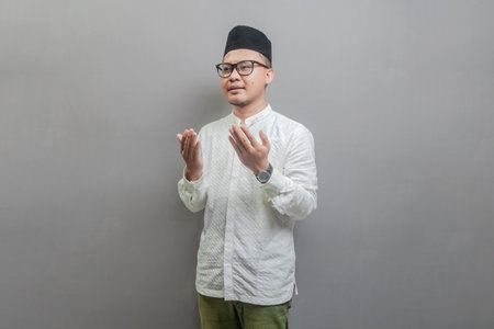 Asian Muslim man wearing a koko shirt and peci with shades of the fasting month, standing looking empty space happily to show grateful , isolated on a gray backgroundの写真素材