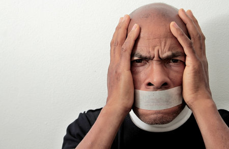 black Caribbean men feeling the pain after being discriminated with tape over his mouth on white background stock photoの写真素材