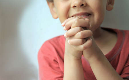 boy praying to God with hands held together with closed eyes on white background stock photo