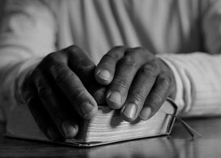 man praying with hand on bible black background stock photo