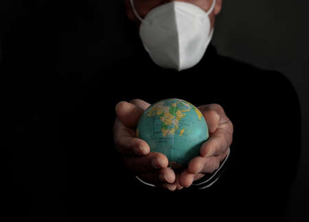 Man in a medical mask holds a globe in his hands on a dark background.の写真素材