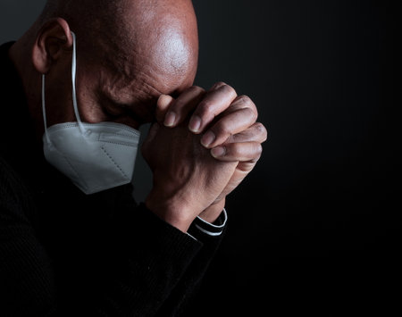 man praying to God with face mask on black background stock photoの写真素材