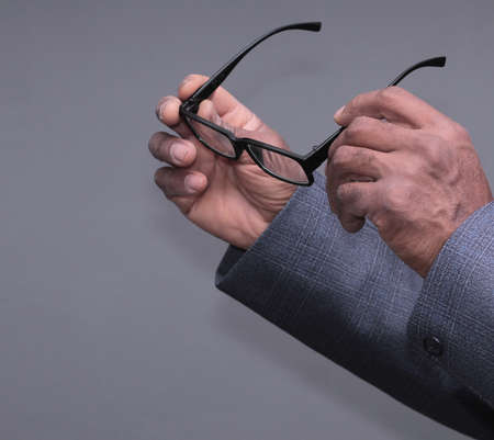 Close-up Of A Businessman's Hand Holding Glasses Against Gray Backgroundの写真素材