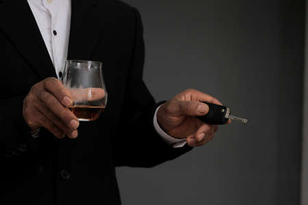 Man with glass of whiskey and car key on grey background, closeupの写真素材