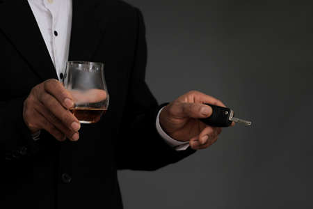Man with glass of whiskey and car key on grey background, closeup. Space for textの写真素材