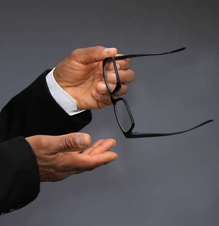 Close-up Of A Businessman's Hand Holding Glasses On Gray Backgroundの写真素材