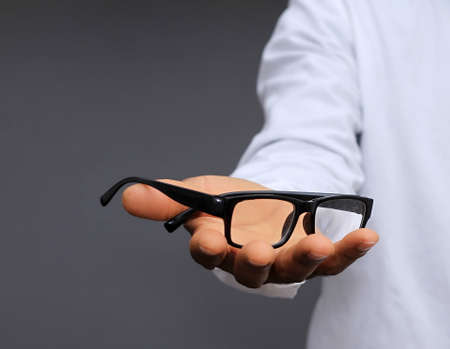 Man holding eyeglasses on grey background, closeup. Space for text