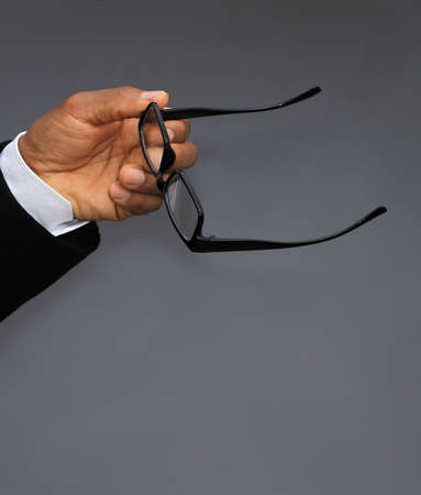 Close-up Of A Businessman's Hand Holding Glasses On Gray Backgroundの写真素材