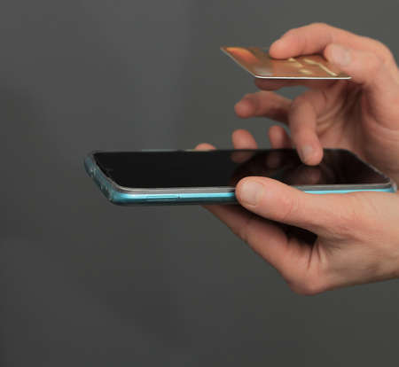 Man holding smartphone and credit card on grey background, closeup. Online shoppingの写真素材