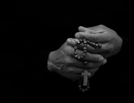 Hands of an old man with a cross on a black backgroundの写真素材