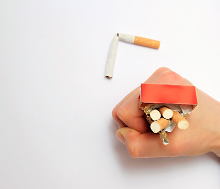 Female hand breaking a cigarette with a red label on a white backgroundの写真素材