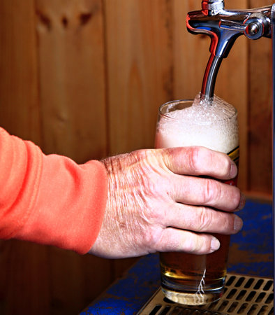 hand pouring beer into a glass on a wooden background, close-upの写真素材