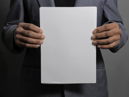 Businessman holding a blank sheet of paper on a gray background.の写真素材