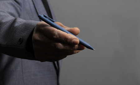 Businessman's hand holding a blue pen on a gray background.の写真素材