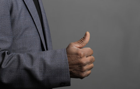 Businessman showing thumbs up gesture on grey background, close-upの写真素材