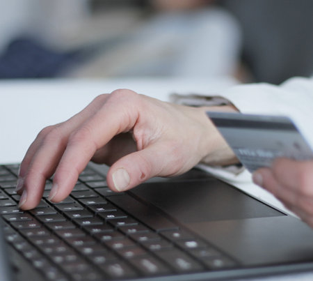 Close-up of woman's hands holding credit card and using laptop computerの写真素材