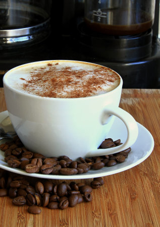 Cup of cappuccino with coffee beans on wooden tableの写真素材