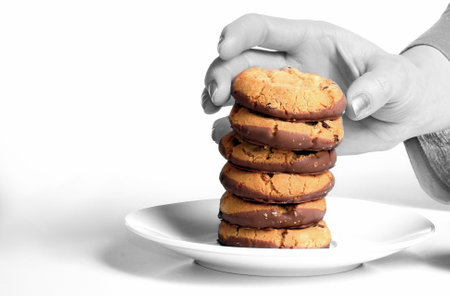 Woman's hand holding a stack of chocolate chip cookies on a white plateの写真素材