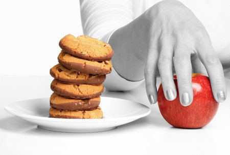 Woman's hand holding a red apple and a stack of cookies.の写真素材