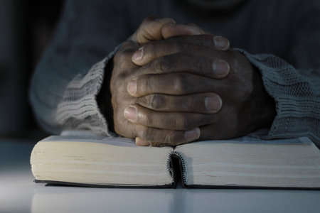 Close up of hands of an old man sitting on a book and praying
