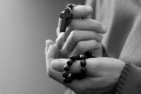 Female hands with a rosary beads and a cross in black and white