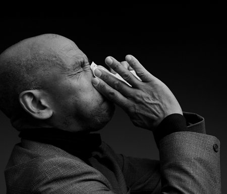 Black and white portrait of a bald man sneezing into a tissue