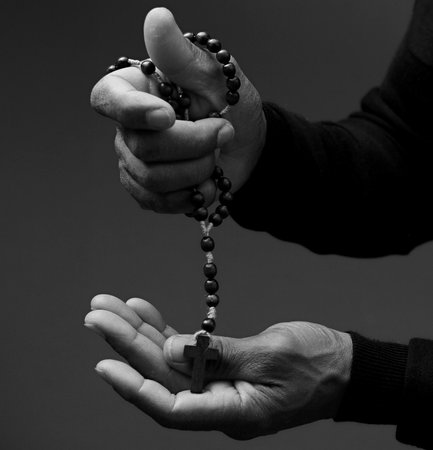 Black and white photo of hands with rosary beads over dark background