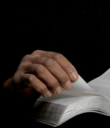 Close up of an old man reading a bible on black background.