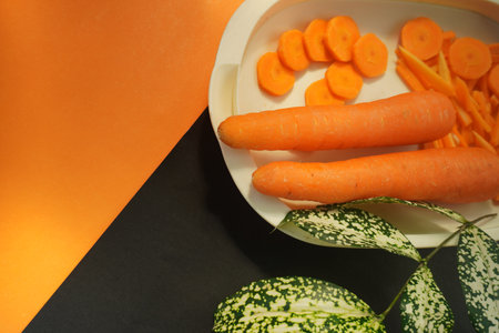 Fresh carrots in a white plate on a black and orange background.の写真素材