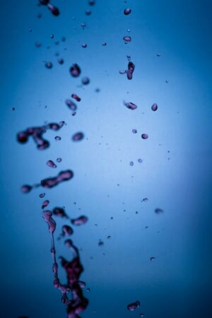 Flying red wine droplets with blue gradient background. Liquid, macro.の写真素材