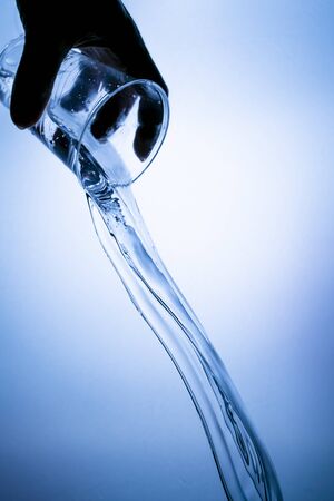 Hand holding a plastic glass with a water splash on a blue backgroundの写真素材