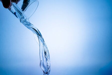 Hand holding a glass with a water splash on a blue backgroundの写真素材