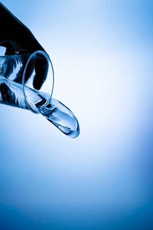 Hand holding a glass with a water splash on a blue gradient backgroundの写真素材