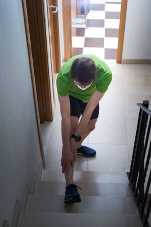 sporty man stretching his legs inside the house with a mask, stay homeの写真素材