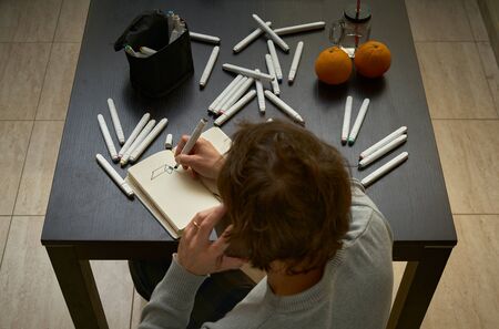 male designer talks on the phone while drawing on a sketchbook on a table with markers and some...