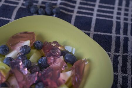 Detail of Fresh fruit salad and red fruit jelly in a green dish on a blue cloth, close upの写真素材