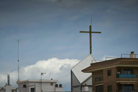 The cross at the top of the modern church tower inside a city, from my windowの写真素材